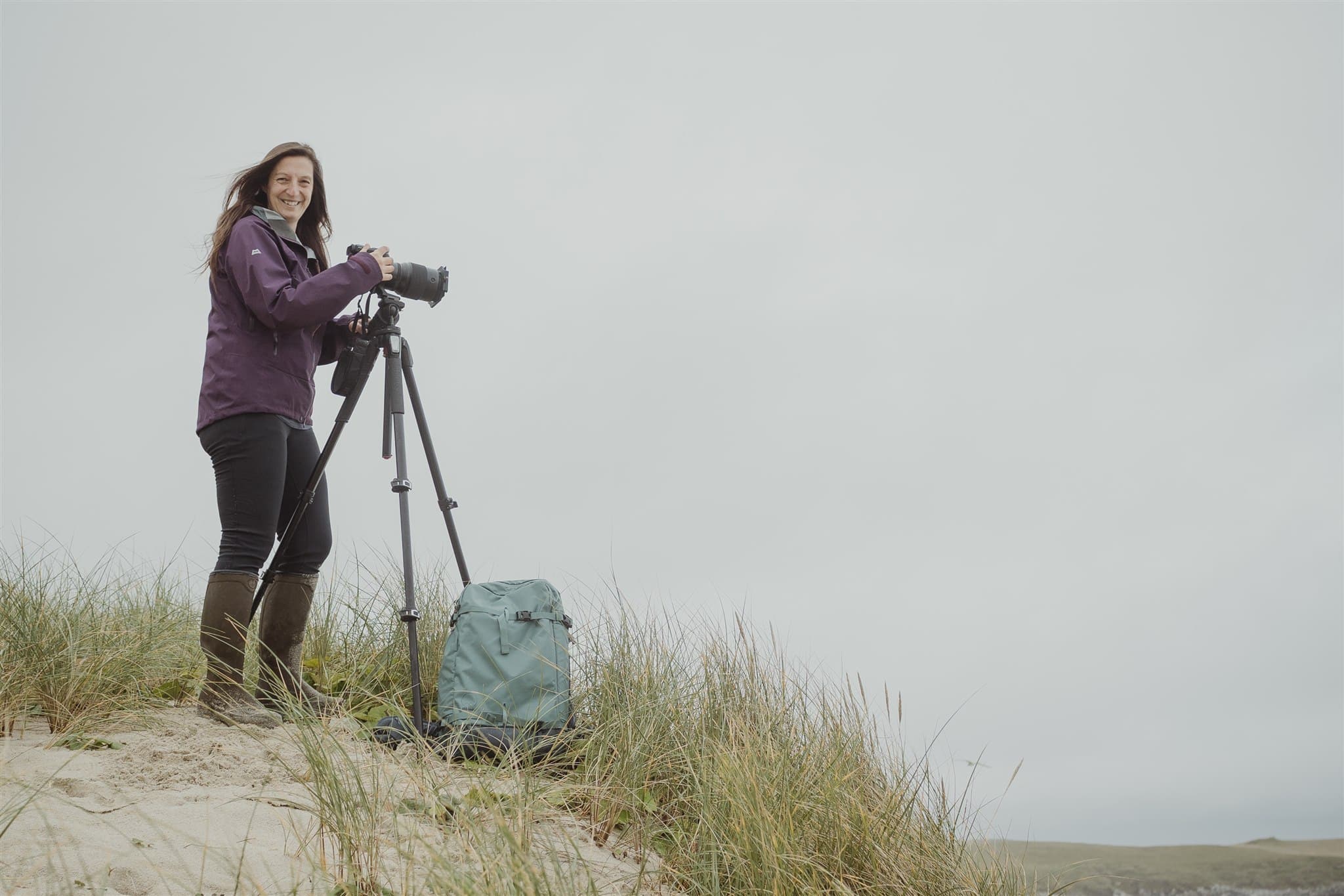 Isle of Harris photographer Margaret Soraya holding a camera and standing on the beach. Margaret offers one to one tuition and creative mentoring.