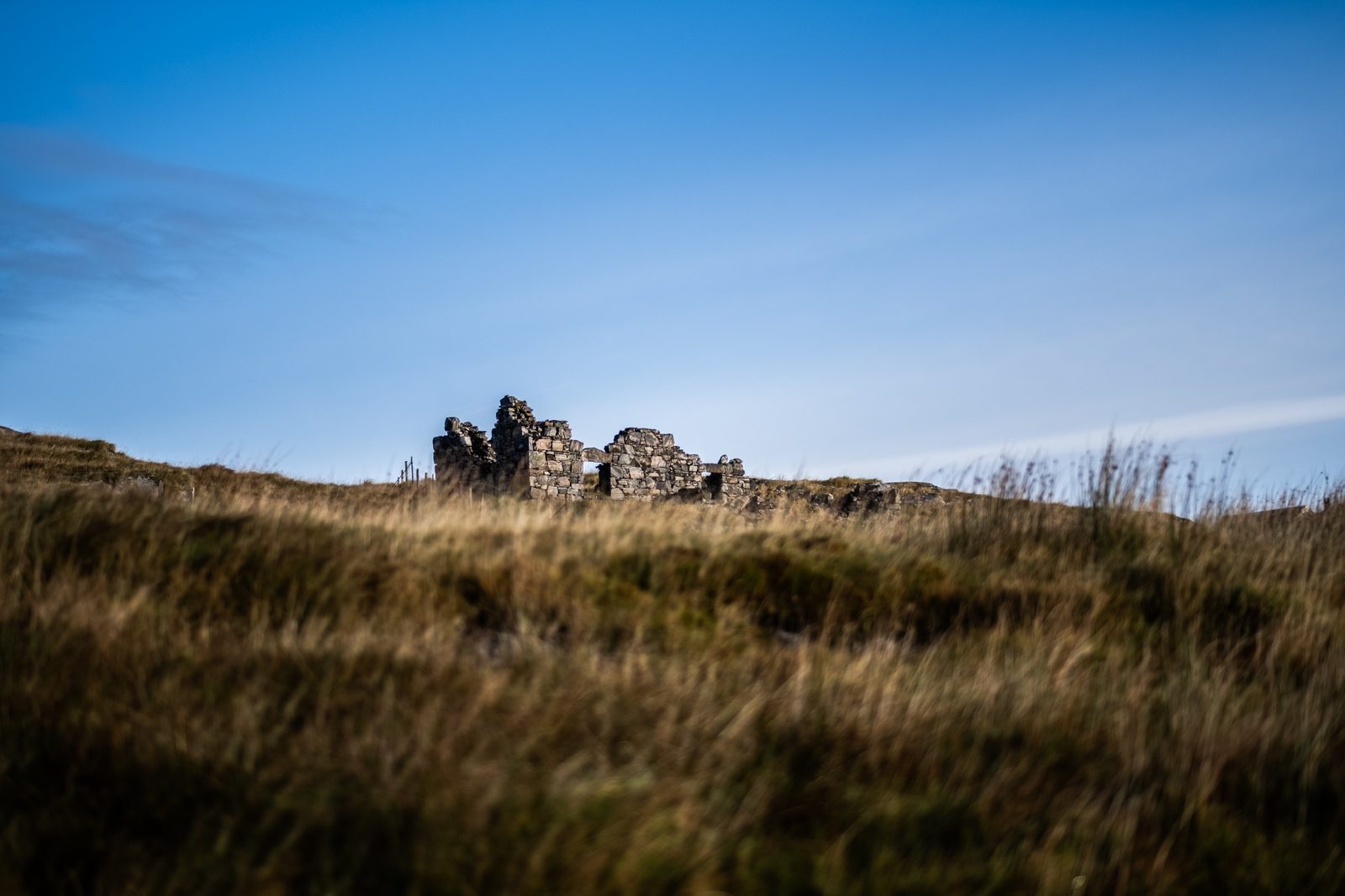 Ruined stone croft buildings on a grassy hillside under blue sky on the Isle of Harris